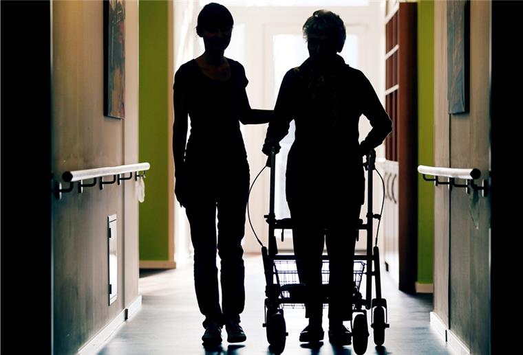 Bremer Forscher: Ein Drittel mehr Personal in der Pflege notwendig Eine Pflegekraft begleitet die Bewohnerin eines Altenheims beim Gang über den Flur.