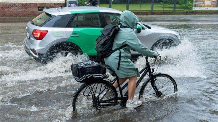 Eine Radfahrerin und ein Auto fahren im Schritttempo durch die überflutete Zeppelinstraße.