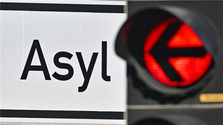 Eine rote Ampel leuchtet vor dem Wort „Asyl“ auf einem Wegweiser zur Erstaufnahme-Einrichtungen (EAE).