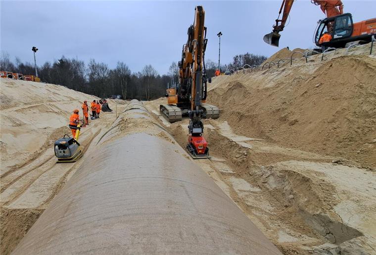 A27-Update zu den Bauarbeiten: So ist der aktuelle Stand Eine Rüttelplatte wird von einem Bauarbeiter gezogen, die andere von einem Bagger: Schicht für Schicht wird der Sand um das neue Rohr verdichtet.