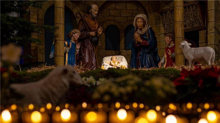 Eine Weihnachtskrippe steht im Osnabrücker Dom hinter brennenden Kerzen.