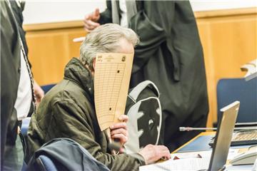 Einer der fünf Angeklagten hält sich im Gerichtssaal eine Mappe vor das Gesicht, um nicht erkannt zu werden. 