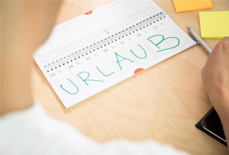  Ein Mann schaut in einen Terminkalender. Dort ist das Wort "Urlaub" in Großbuchstaben zu lesen.  Einfach so mehr Geld zum Urlaub? Das geht – wenn du Anspruch auf Urlaubsgeld hast. Wie du das herausfindest und warum auch Gewohnheit zum Recht werden kann.