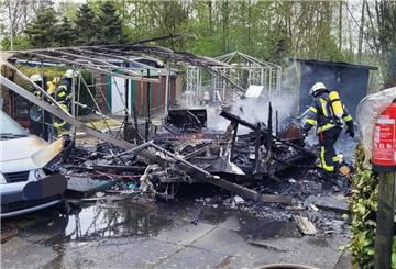 Einsatzkräfte der Feuerwehr während der Nachlöscharbeiten am völlig niedergebrannten Wohnwagen.