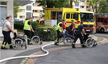 Einsatzkräfte schieben leere Rollstühle aus dem Pflege- und Altenheim. Das gesamte Dach des Heims ist abgebrannt. 


