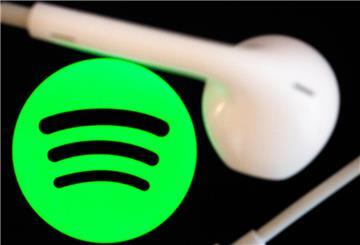  Kopfhörer liegen auf dem Bildschirm eines Smartphones, auf dem das Logo vom Musikstreaming-Dienst Spotify angezeigt wird. 