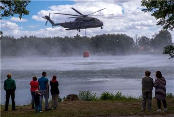 Einwohner und Urlauber beobachten einen Hubschrauber CH53 der Bundeswehr beim Aufnehmen von 5000 Liter Löschwasser in einem See. 

