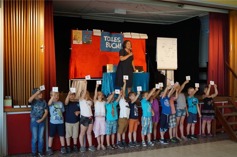 „Ella in der Schule“, ergeben die Buchstaben, die die Jungen und Mädchen der Grundschule Abbehausen nach oben halten. Das war der Titel eines der sechs Bücher, die  Tina Kemnitz den Grundschülern vorstellte. 
