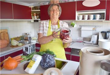 Eine Frau steht in ihrer Küche mit Gemüse in der Hand.