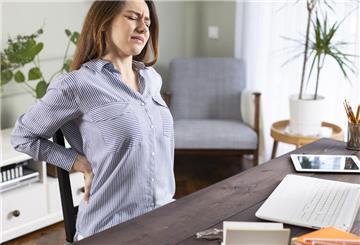 Freelancer young woman suffering with back pain while working in her office at home