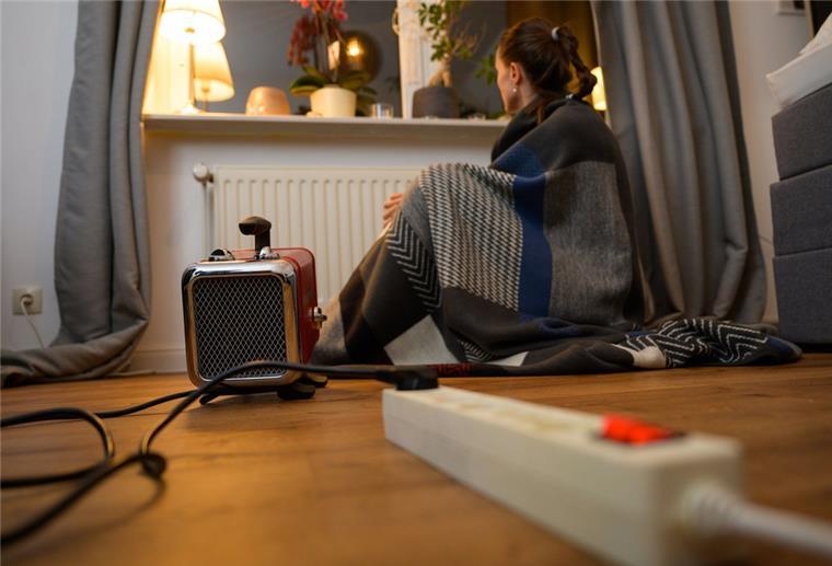 Feuerwehr: Elektroheizungen können brandgefährlich sein Ein Frau sitzt mit einer umgehangenen Decke hinter einem Elektro-Heizlüfter.