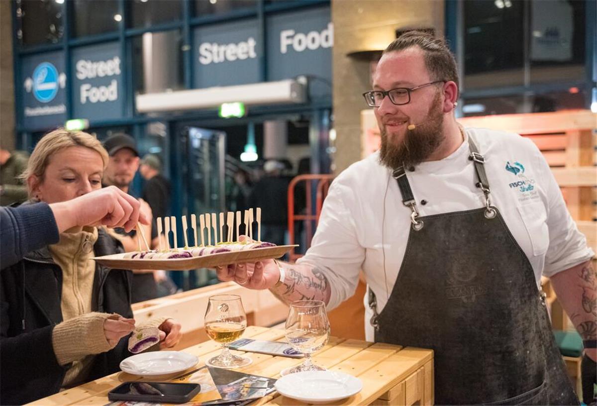 „Foodpairing Fisch und Bier“ - jetzt Tickets sichern! Fischsommelier Ralf Harms reicht Teilnehmern im Fischkochstudio Bremerhaven Häppchen.