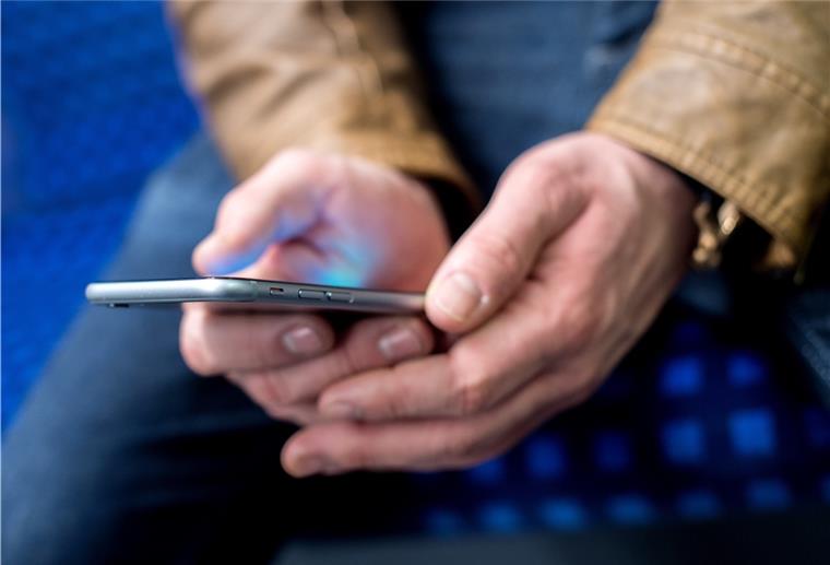 Achtung!!! Kriminelle SMS-Benachrichtigungen für Pakete Ein junger Mann sitzt in einer S-Bahn und benutzt dabei sein Smartphone.