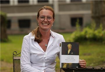 Das Foto zeigt Esther Meyer-Biemold vor dem Jagdschloss mit einer Biografie in der Hand.  