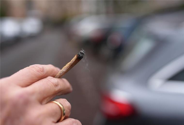 Mischkonsum am Steuer - Strengere Regeln für Cannabis gefordert Ein Mann hält einen Joint auf einer Straße.