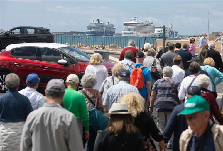 Menschen und Fahrzeuge überqueren einen Zebrastreifen vor dem Hafen von Palma, wo Kreuzfahrtschiffe vor Anker liegen.