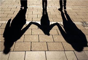 Die Schatten von zwei Erwachsenen und einem Kind fallen in den Morgenstunden auf den Asphalt.