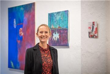 Frau steht vor einer Wand mit Acrylbildern und lächelt.