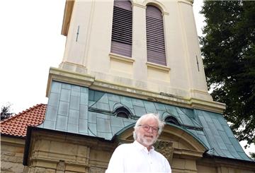 Mann mit Bart und Brille vor Kirchturm