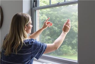 Junge Frau steht am Fenster und bringt eine Folie an.
