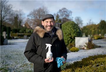 Frank Becker steht mit einer Sprühflasche und einem Lappen in der Hand auf dem Friedhof in Wulsdorf.