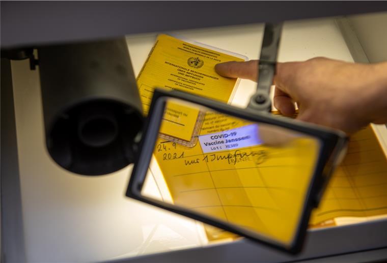 Gefälschter Impfpass - Stader Polizisten unter Verdacht Bei der Kriminalpolizeiinspektion liegen Impfpässe unter einer Lupe, darunter ein aufgeschlagener Impfausweis mit einem Eintrag einer Corona-Impfung mit dem Impfstoff Johnson & Johnson.