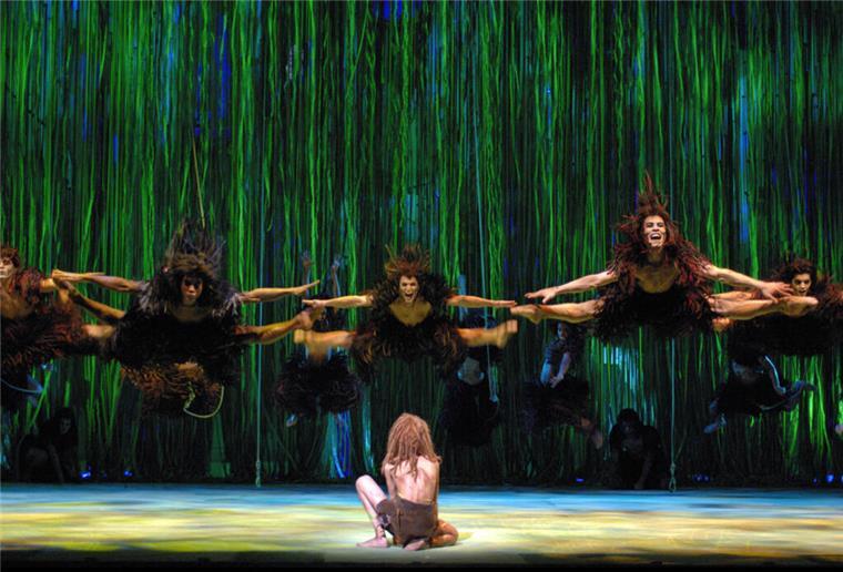 Junge Talente aufgepasst: Tarzan-Casting in Hamburg Ein Tarzan-Darsteller kniet auf der Bühne. Vor ihm springen weitere Darsteller in die Luft.