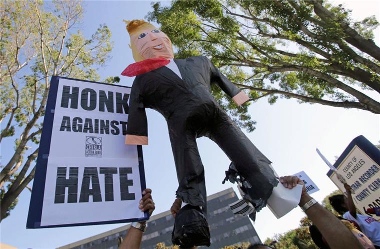 Trump und die Furcht vor dem dunklen Amerika Gegner von Donald Trump halten ein Schild mit der Aufforderung "Hupe gegen Hass" und eine aufblasbare Puppe, die Donald Trump darstellt, in die Höhe.
