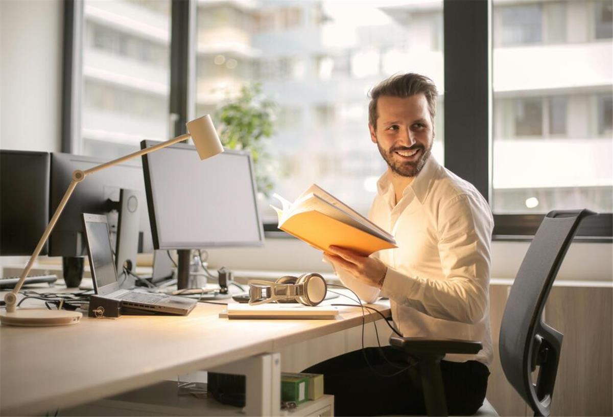 Auswirkungen der Pflicht zur E-Rechnungsstellung auf norddeutsche Unternehmen Ein junger Mann im weißen Hemd sitzt am Schreibtisch vor einem Computer und blättert in einem Notizbuch.