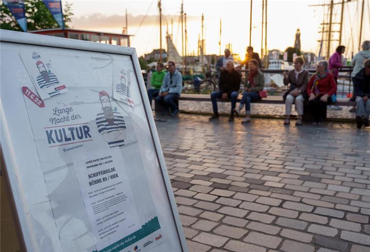Ein Plakat der Langen Nacht der Kultur Bremerhaven. Im Hintergrund sitzen Menschen bei Sonnenuntergang.