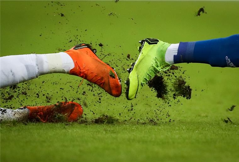 Fußball auf Kreisebene abgesagt Gras fliegt um die Fußballschuhe zweier Spieler bei einem Zweikampf.