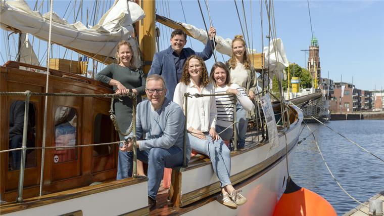 Mehrere Menschen stehen lächelnd auf einem Boot im Becken des Neuen Hafens Bremerhaven. 