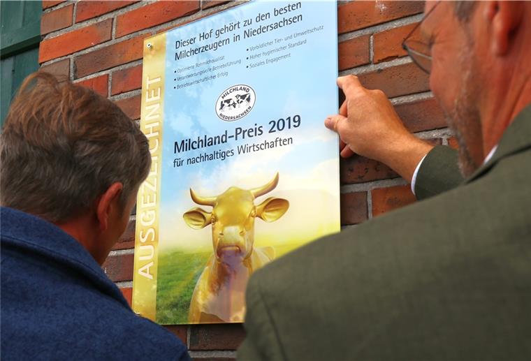 Preis für vorbildliche Landwirtschaft Hartwig Gloystein (links) und Jan Heusmann, Vorstand der Landesvereinigung Milchwirtschaft in Niedersachsen, montieren die Auszeichnung am Stallgebäude.