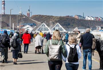 Helgoland-Besucher gehen nach ihrer Ankunft per Schiff über die Hafenstraße Richtung Inselzentrum.