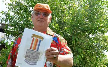 Henk Tijink, Moderator und Mit-Organisator der Vier-Abend-Märsche in Zeven, schreckt vor schrillen Outfits nicht zurück, um der Veranstaltung Aufmerksamkeit  zu sichern. Hier zeigt er ein Bild der Medaille, die die Teilnehmer bekommen, die an mindestens drei der vier Abende mitlaufen. 