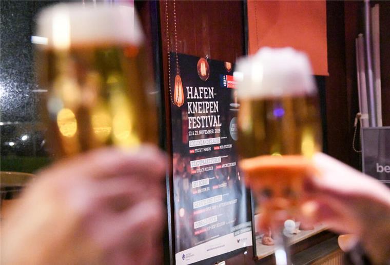 Seele der Stadt am Tresen: Hafenkneipenfestival in Bremerhaven Ein volles Bierglas wird vor einem Plakat in die Höhe gehalten.