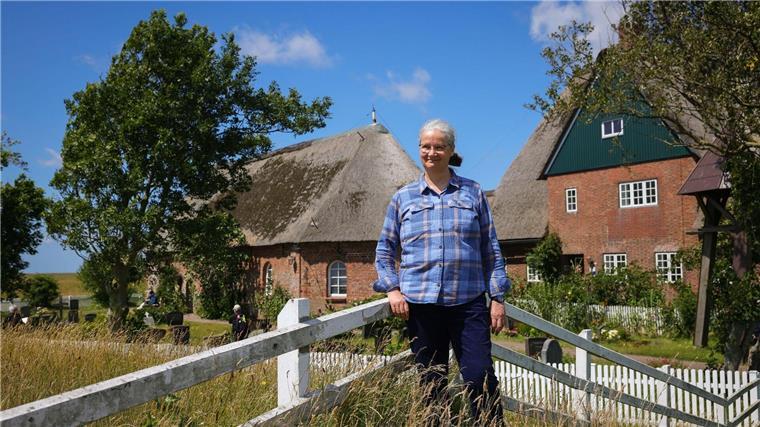 Am Ende des Berufsleben etwas Neues gewagt Hildegard Rugenstein, Pastorin auf der Hallig Hooge, steht auf der Kirchwarft vor dem Pastorat (r) und der St. Johannis Kirche (l).