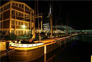 Ein Holzschiff liegt bei Nacht vor dem Koggenbräu-Gebäude in Bremerhaven.