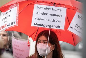 Eine Demonstrantin trägt bei einem Protestmarsch durch die Friedberger Innenstadt einen Regenschirm mit einem Plakat und der Aufschrift "Wer eine Horde Kinder managt verdient auch ein Managergehalt".