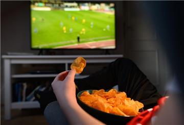 Ein Junge sitzt vor dem Fernseher und ist Kartoffelchips.