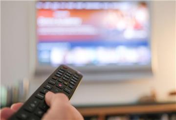 Eine Hand bedient eine Fernbedienung für ein TV-Gerät. 