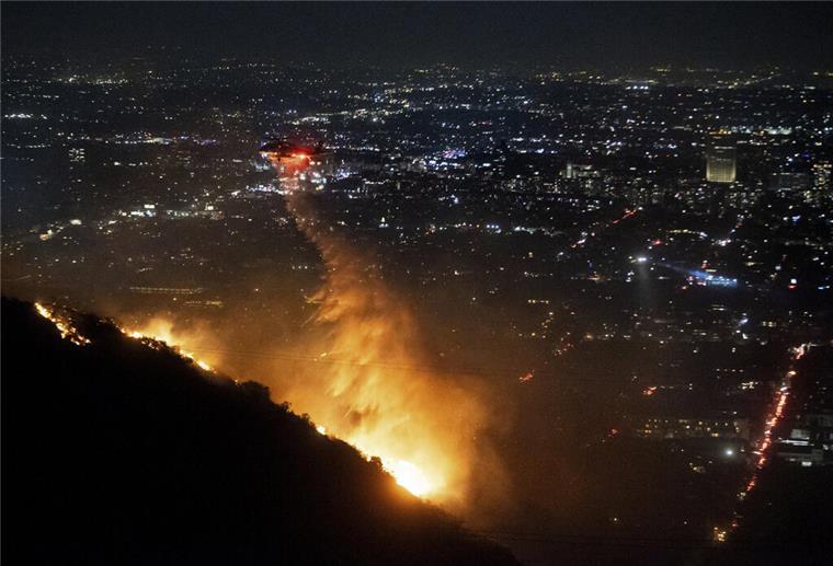 08.01.2025, USA, Los Angeles: Ein Hubschrauber wirft Wasser auf das brennende Sunset Fire in den Hollywood Hills. Foto: Ethan Swope/AP/dpa +++ dpa-Bildfunk +++