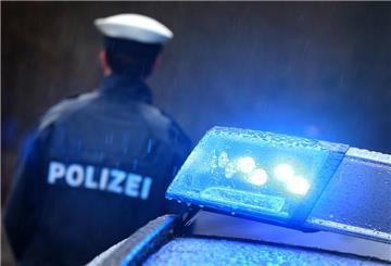 Ein Polizist steht im Regen vor einem Streifenwagen, dessen Blaulicht aktiviert ist.
