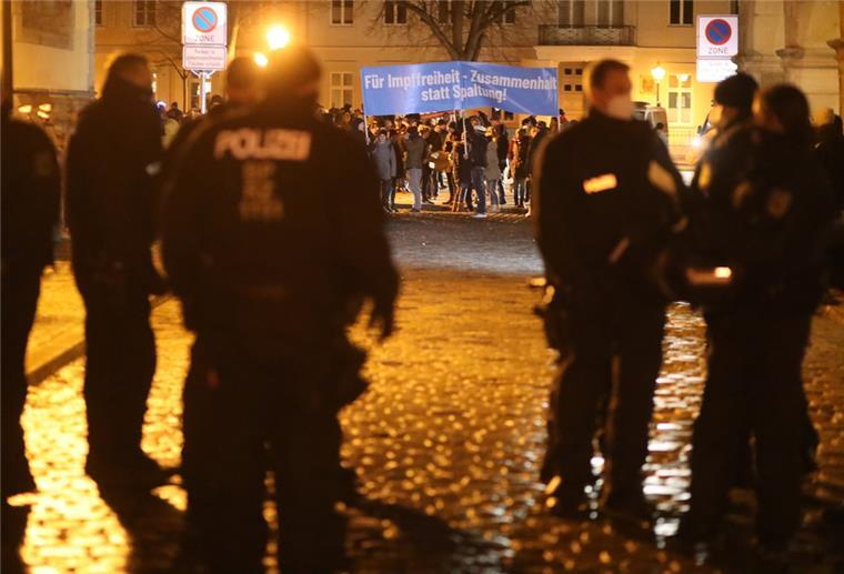 Die Zahl der Corona-Demos ist im April weiter zurückgegangen im Hintergrund demonstrieren Menschen für die Impffreiheit. Im Vordergrund stehen Polizisten.