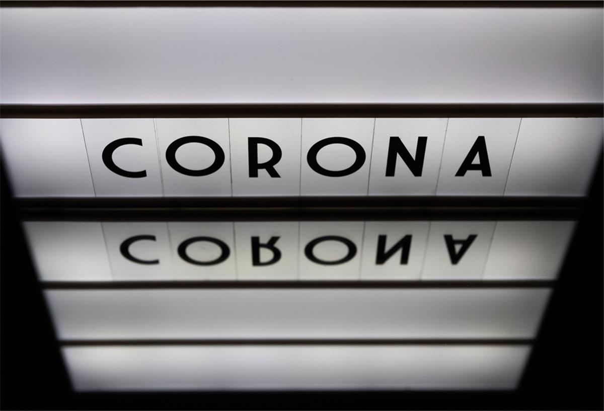 Ein Leuchtkasten mit den Worten Corona, Covid-19, 2020 spiegelt sich in einem Spiegel. (gestellte Szene