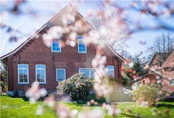 Ein Haus mit einem grünen Garten. Sonnenbaden im eigenen Garten birgt keine gefahren. Sollte man allerdings zu viel Haut zeigen, können Bußgelder drohen.