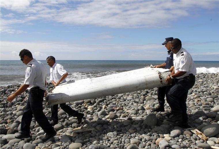 Techniker tragen ein Wrackteil, die Flügelklappe eines Flugzeugs, über einen Strand bei Saint-Andre de la Reunion.
