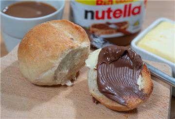 Ein Brötchen mit Nutella liegt auf einem Frühstücksbrett