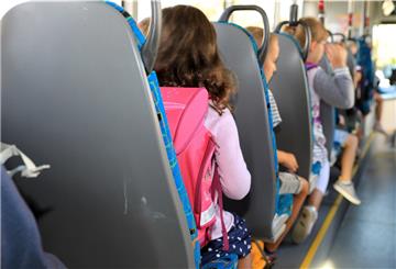 Kinder sitzen mit ihrem Ranzen in einem Schulbus. 