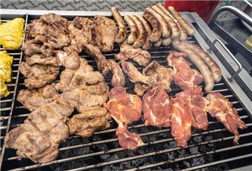  Zahlreiche Fleischstücke und Würste liegen auf einem großen Holzkohlegrill. 